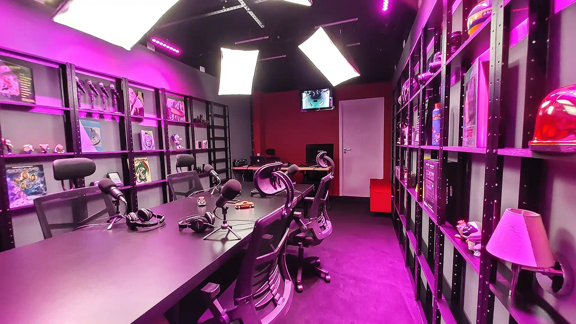 Sala de gravação do Yourcast Estúdio com luzes na ambientação rosa vista diagonal do fundo.